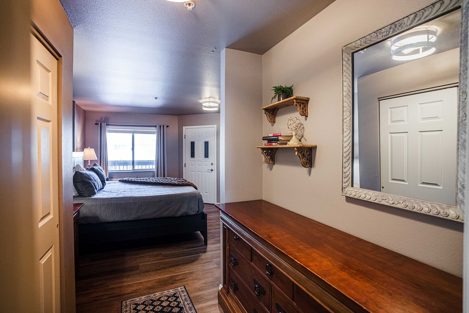 A bedroom with a bed, bedside table, dresser, and a large mirror.