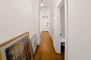 A hallway with wooden flooring, white walls, and a door at the end.