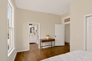 A bedroom with a bed, a wooden floor, a white door, and a bathroom visible through an open door.
