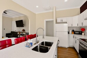 A modern kitchen with white cabinets, a stainless steel sink, and a dining area with red chairs.
