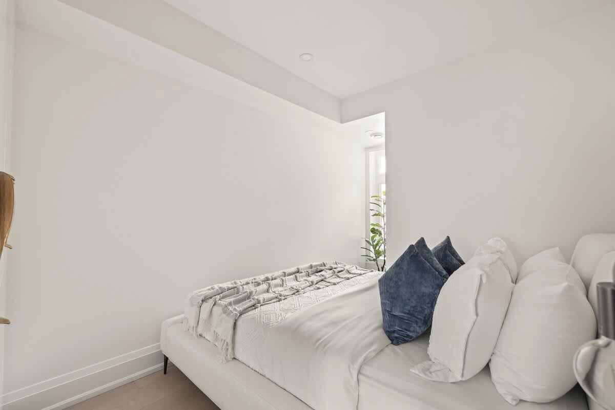 A bedroom with a white bed, a bedside table, and a window with a view.