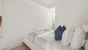 Un dormitorio con cama blanca, mesita de noche y ventana con vistas.