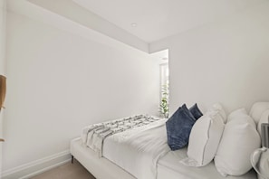 A bedroom with a white bed, a bedside table, and a window with a view. - Stylish West End Apt, Cozy City Retreat! (Toronto)
