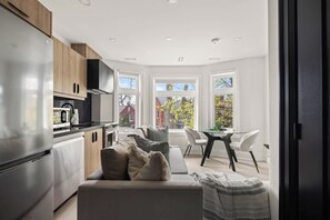 A modern kitchen with a dining area, large windows, and a view of the outside.