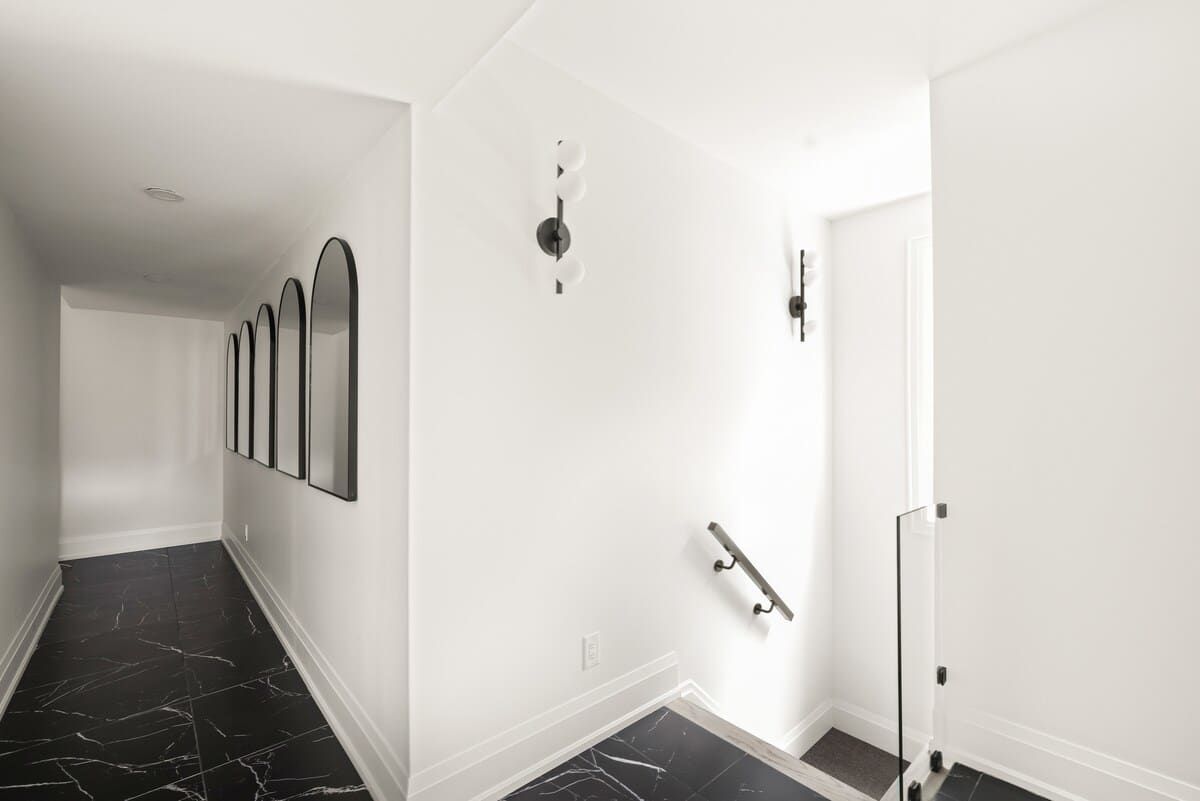 A hallway with a black marble floor, white walls, and a door with a glass door.