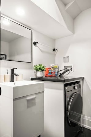 A modern bathroom with a sink, mirror, and washing machine. - Stylish West End Apt, Cozy City Retreat! (Toronto)