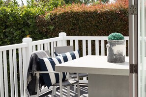 A white deck with a table and chairs, a potted plant, and a hedge in the background. - The Rose Cottage by Homello (Auckland)