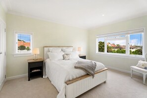 A bedroom with a bed, bedside tables, a nightstand, a window with a view, and a small white bench. - The Rose Cottage by Homello (Auckland)