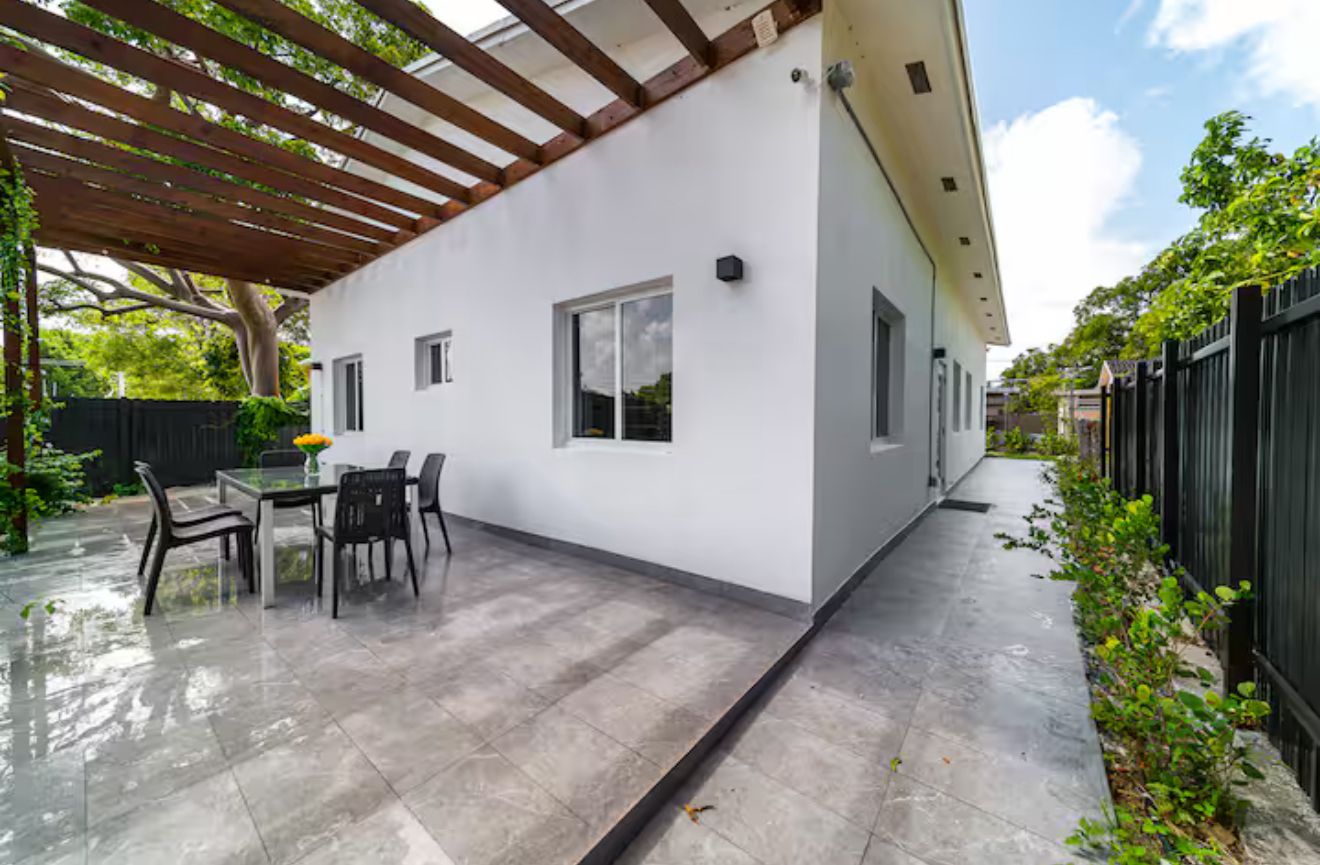Uma casa moderna com um alpendre coberto, uma mesa de jantar com cadeiras e uma pequena janela.