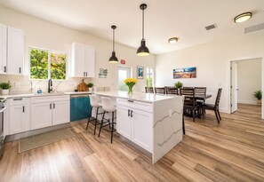 A modern kitchen with white cabinetry, a central island with bar stools, and a dining area with wooden chairs. - Soothing 4-bedroom house with AC in Hallandale Beach (Hallandale Beach)