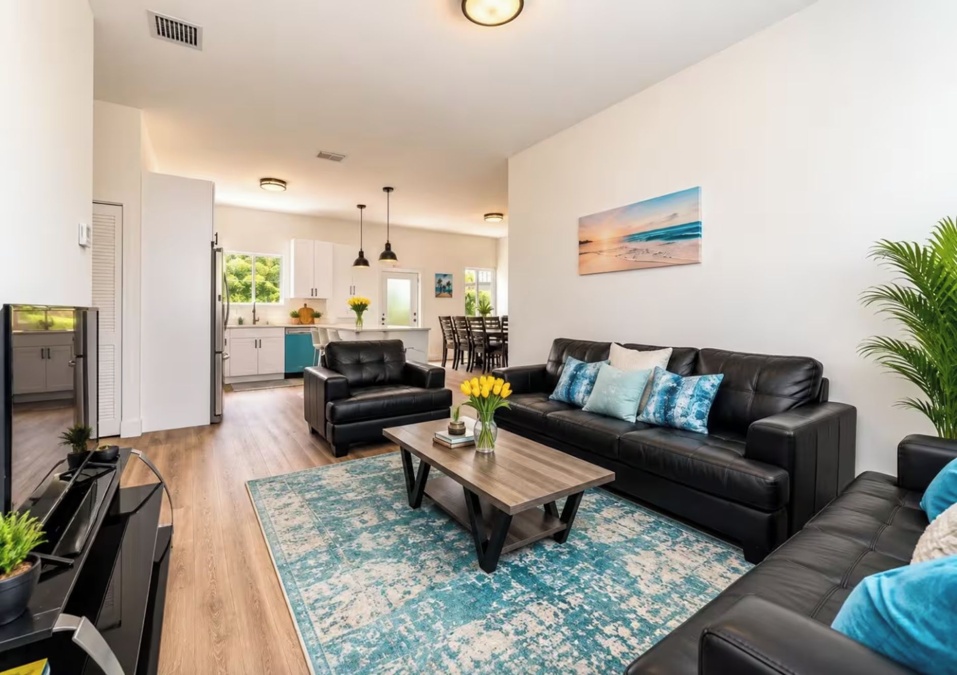 A modern living room with a black leather sofa, a wooden coffee table, and a blue patterned rug.