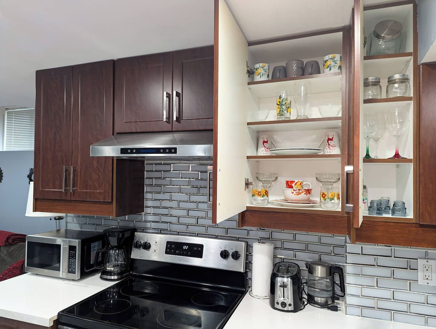 A kitchen with dark wooden cabinets, a stainless steel range hood, a microwave, a toaster, and a coffee maker.