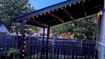 A covered patio area with string lights, wooden railings, and potted plants.