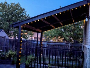 A covered patio area with string lights, wooden railings, and potted plants.