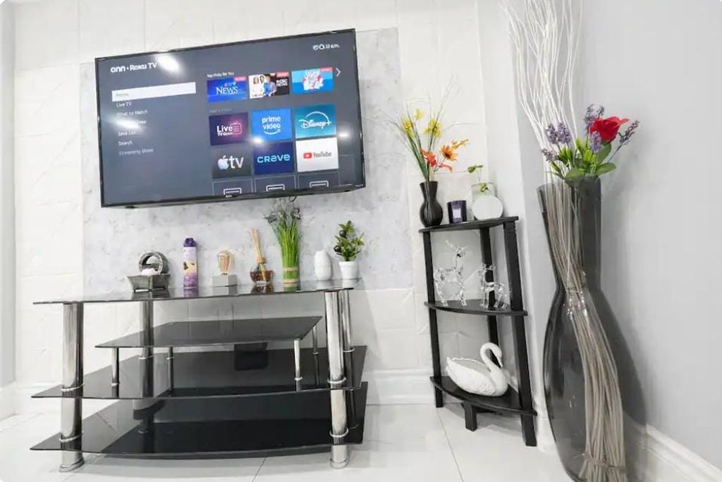 A modern living room with a flat-screen TV mounted on a white wall, a black entertainment unit below, and a vase with flowers on a side table.