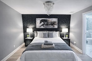 Une chambre à coucher moderne avec un grand lit, deux tables de chevet avec des lampes, un lustre et une œuvre d’art accrochée au mur.