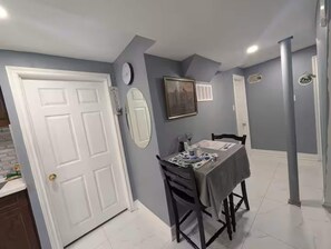 Un coin repas avec une table dressée pour deux personnes, une horloge au mur et un tableau encadré.