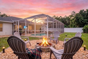 A backyard with a fire pit, outdoor seating, a pool, and a covered patio area. - Saltwater Pool Solar Heated | Fenced | FirePit | Ping Pong (Palm Coast)