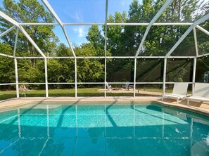 En swimmingpool med ett klart, blått vatten, omgiven av ett vitt metallstaket, och träd i bakgrunden.