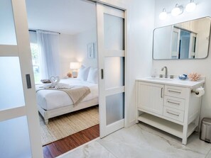 A bedroom with a bed, a bedside table, a nightstand, and a window with curtains. - Saltwater Pool Solar Heated | Fenced | FirePit | Ping Pong (Palm Coast)