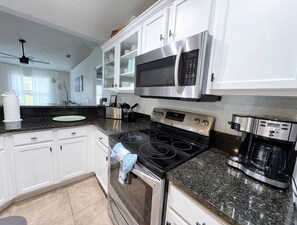 A modern kitchen with white cabinets, a stainless steel microwave, a gas stove, and a coffee maker. - Saltwater Pool Solar Heated | Fenced | FirePit | Ping Pong (Palm Coast)