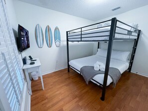 Ein Schlafraum mit Etagenbett, Schreibtisch, Fernseher und Surfbrettdrucken.