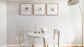 Un'area pranzo minimalista con un tavolo rotondo, due sedie, un vaso con fiori e una lampada da terra.