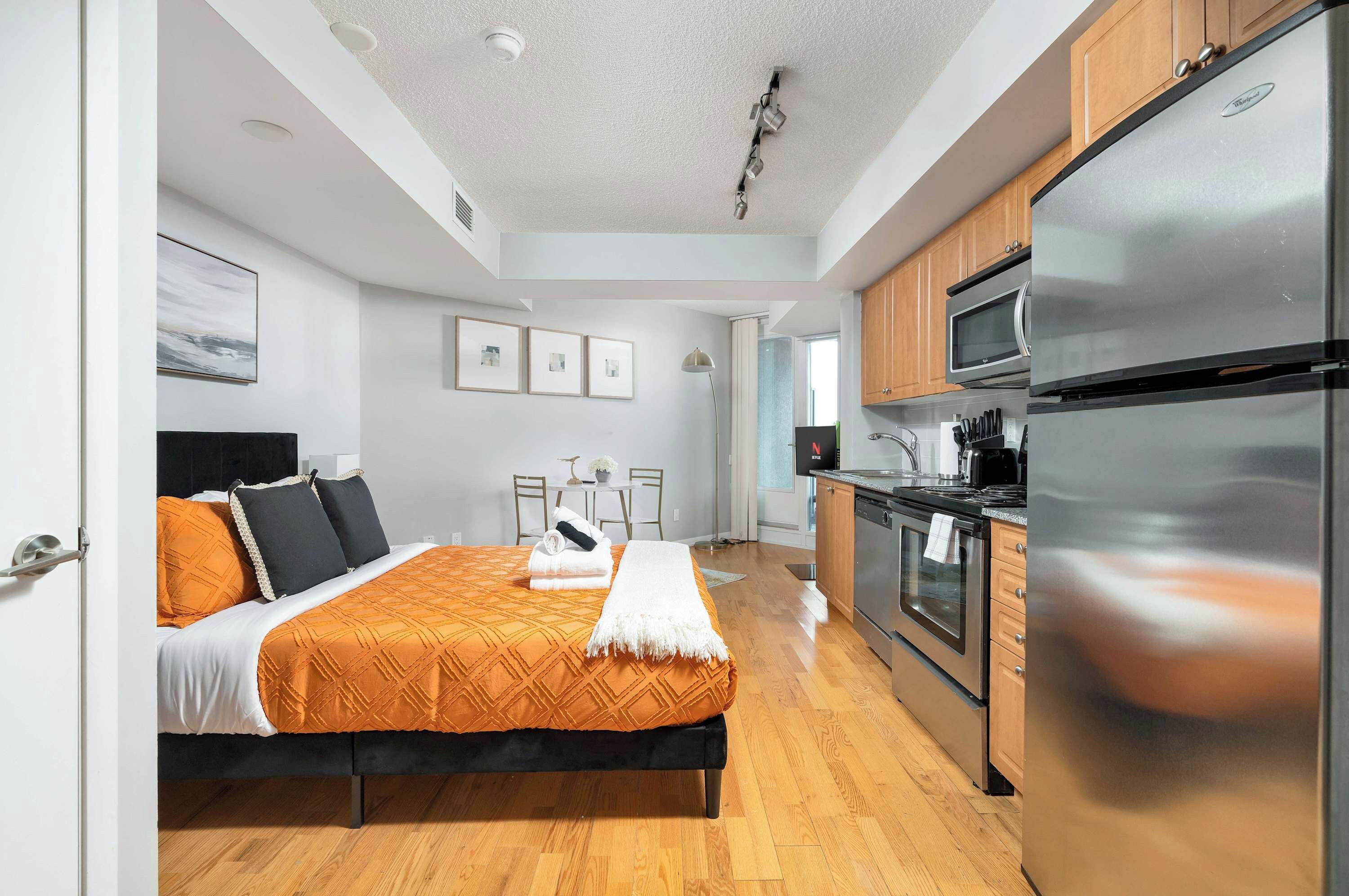 A modern hotel room with a bed, a kitchenette, and a bathroom.
