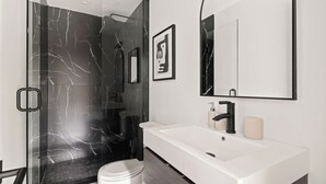 Un baño moderno con ducha acristalada, lavamanos blanco y un espejo grande.