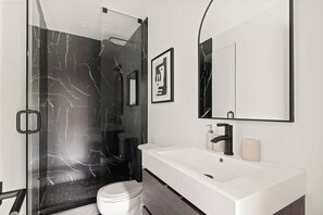 A modern bathroom with a glass-enclosed shower, a white sink, and a large mirror. - Bright West End Gem, Walk to Waterfront! (Toronto)