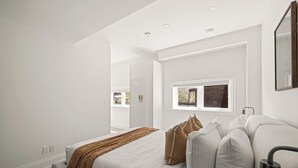 Un dormitorio moderno con cama, paredes blancas, una ventana y un espejo.
