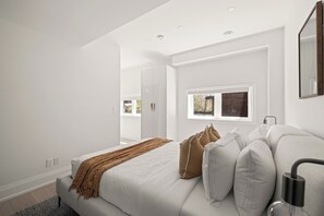 A modern bedroom with a bed, white walls, a window, and a mirror. - Bright West End Gem, Walk to Waterfront! (Toronto)