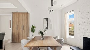 Un comedor moderno con una mesa de madera, sillas blancas, un florero con flores y un cuadro abstracto grande en la pared.