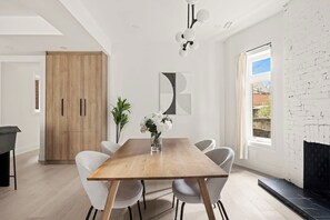 A modern dining area with a wooden table, white chairs, a vase with flowers, and a large abstract painting on the wall. - Bright West End Gem, Walk to Waterfront! (Toronto)