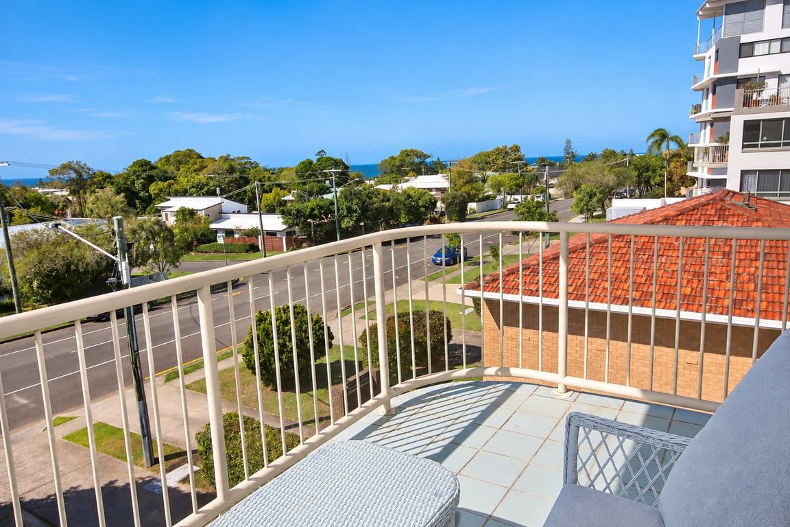 A balcony with a view of a residential area and a building with a red roof.