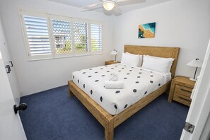 A bedroom with a wooden bed, white bedding, a ceiling fan, and a window with blinds.