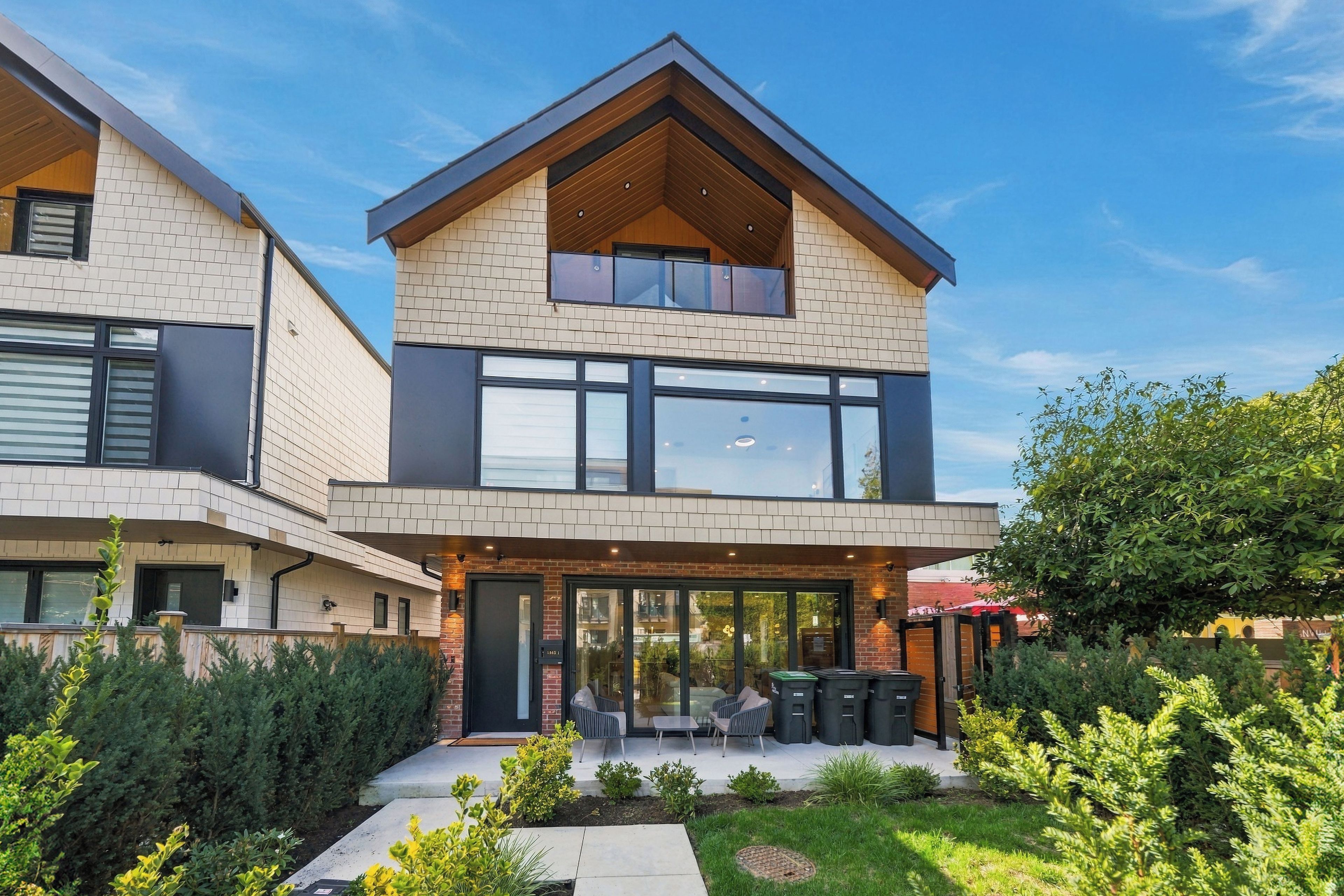 A modern two-story house with a flat roof, large windows, and a balcony.