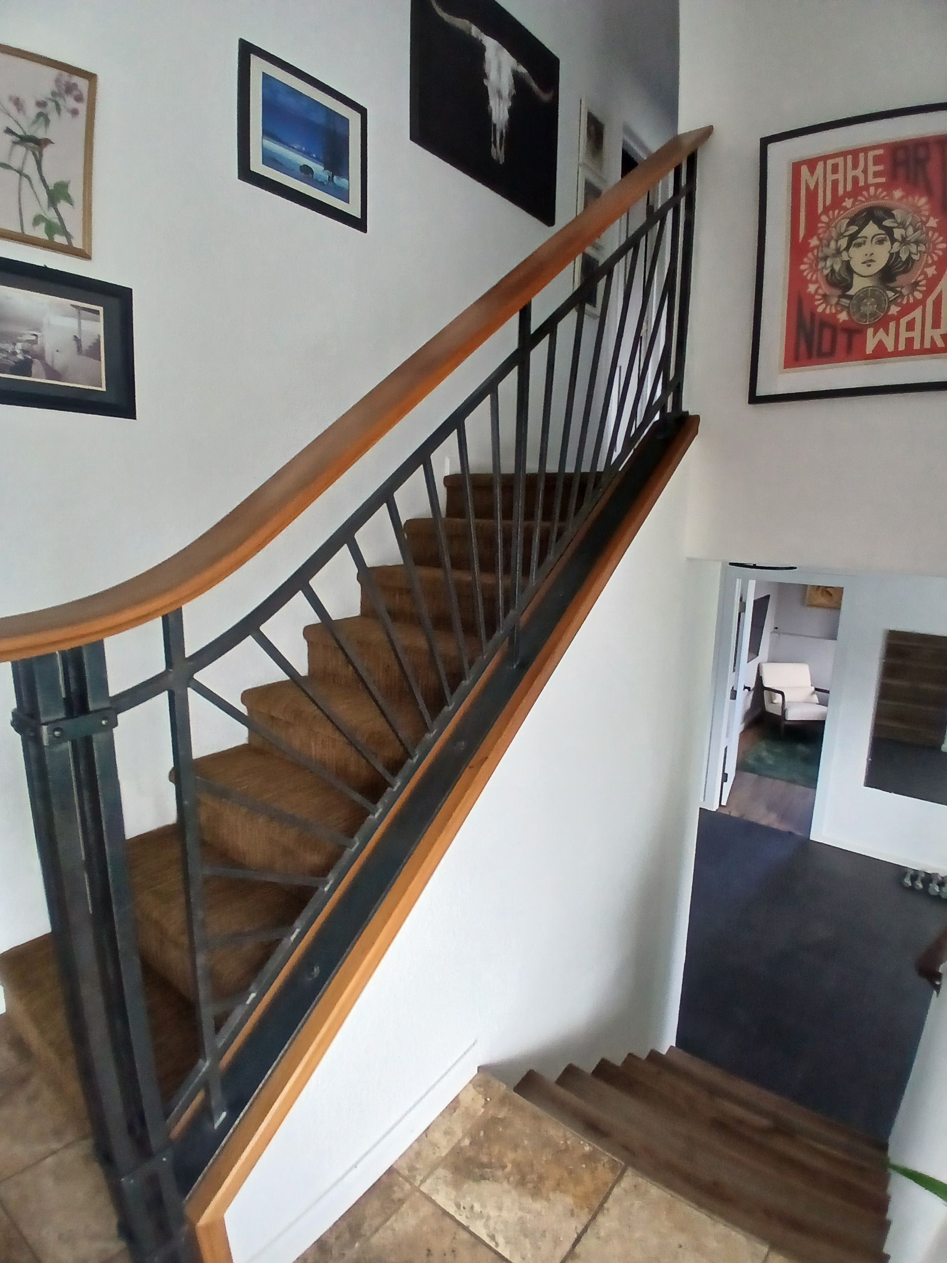 Un escalier avec des marches en bois et des rampes noires, menant à un palier doté d’une porte.