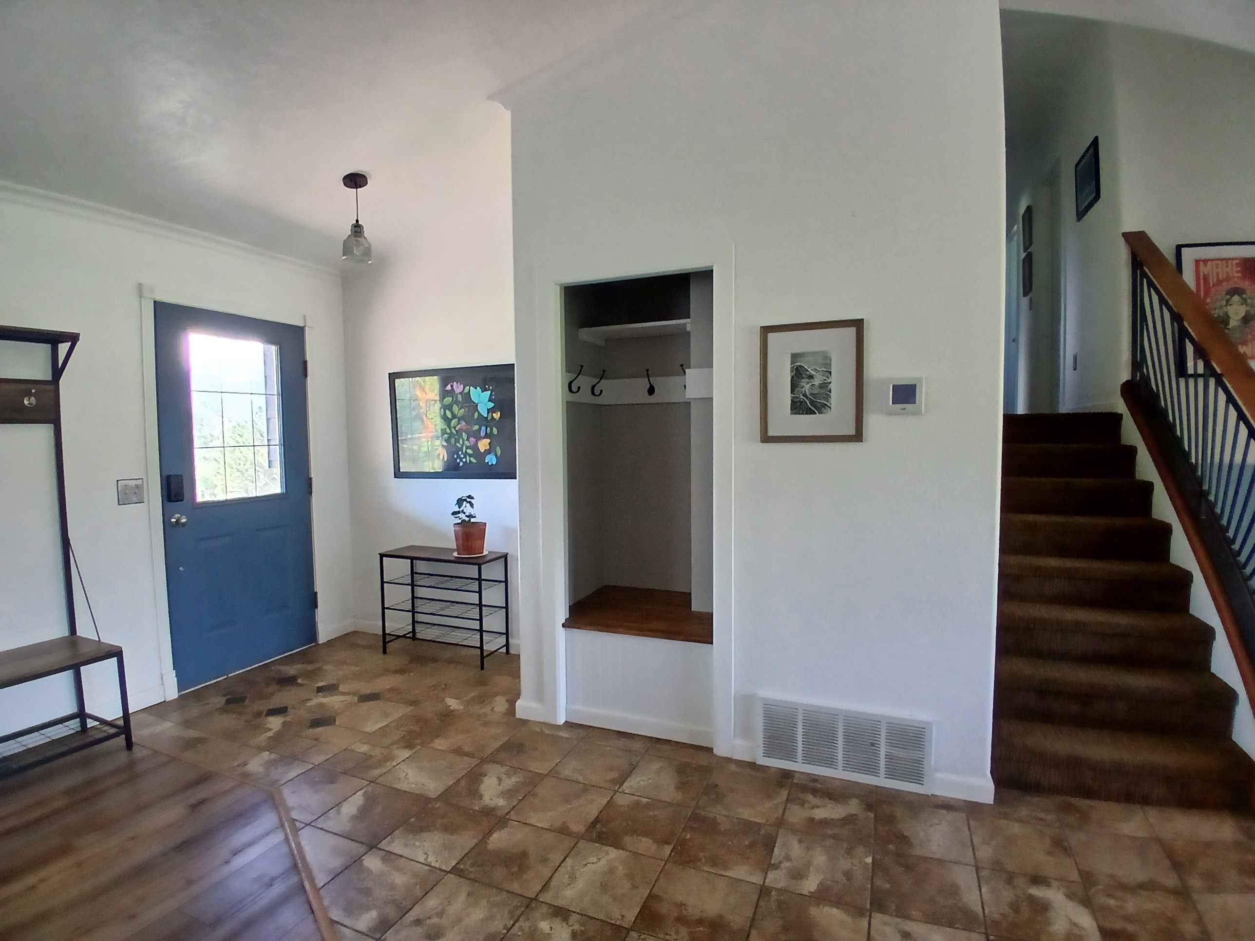Un couloir avec une porte bleue, une petite table sur laquelle est posée une plante en pot, et un escalier avec une rampe en bois.