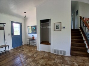 A hallway with a blue door, a small table with a potted plant, and a staircase with a wooden railing.