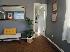 A room with a white bench, a mirror, a potted plant, and a doorway leading to a bathroom.