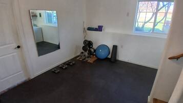 Ein Zimmer mit Tür, Spiegel, Fenster und Trainingsgeräten, darunter Kurzhanteln und einem Medizinball.