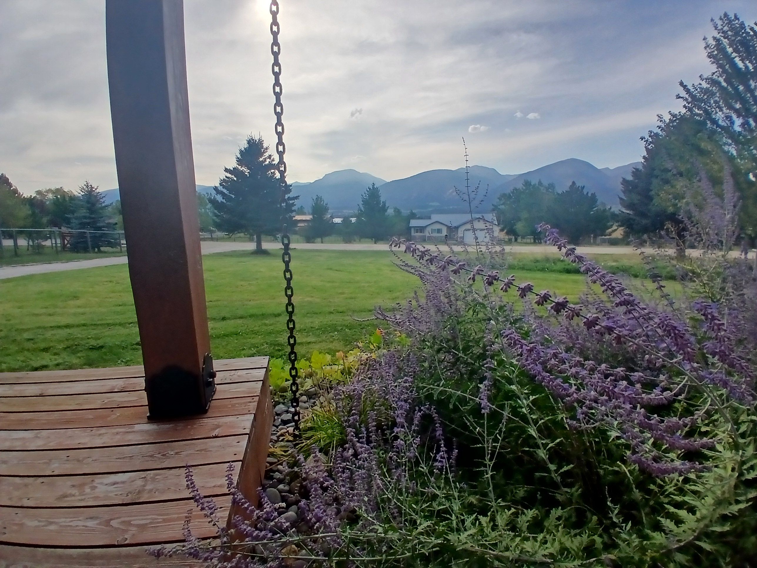 Une terrasse en bois avec une balançoire, entourée de verdure et offrant une vue sur les montagnes lointaines.