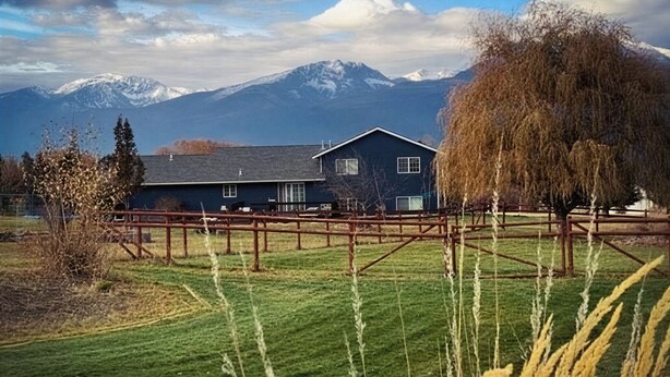 Ett hus med en inhägnad trädgård, ett bergskedja i bakgrunden och en klar himmel.