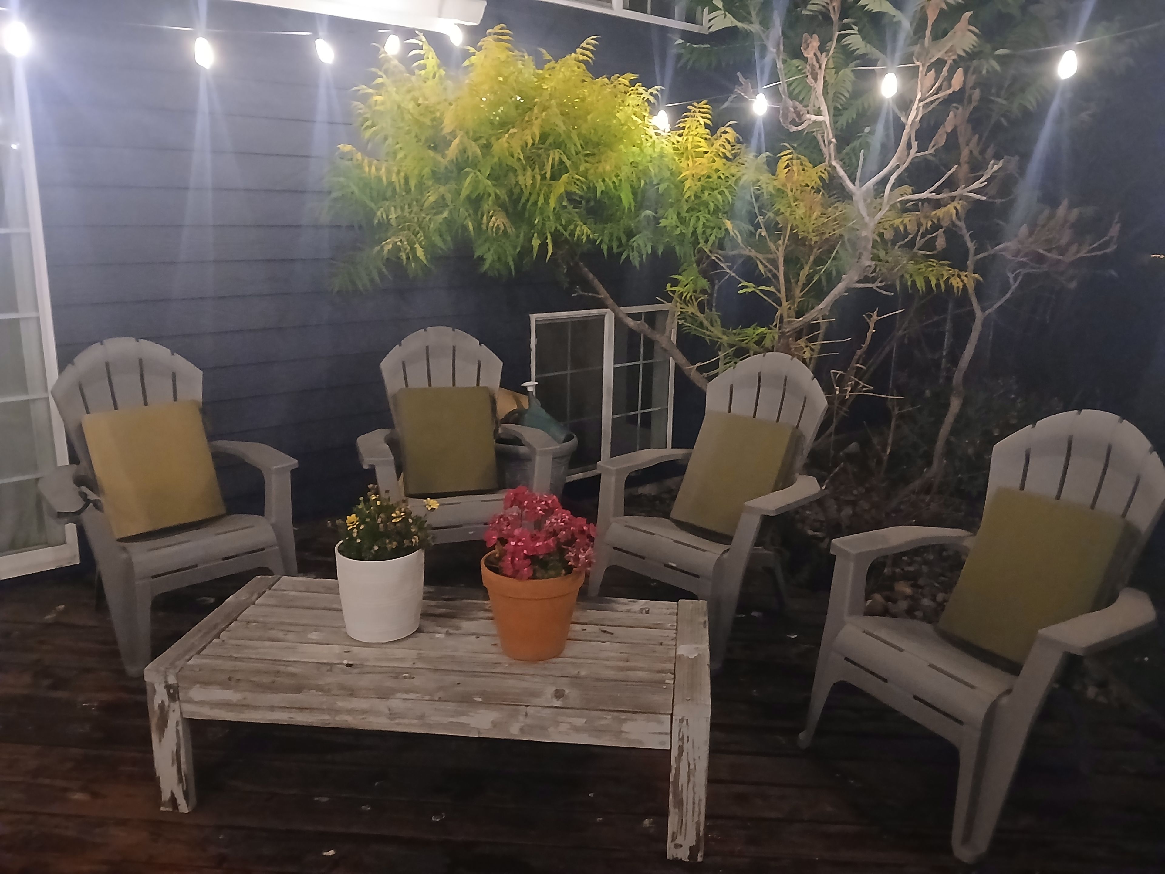 Un espace extérieur aménagé avec quatre fauteuils Adirondack, une table en bois et des plantes en pot.