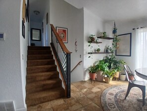 A staircase with a wooden handrail leading to a landing, a dining area with a round table and chairs, and multiple potted plants on shelves. - Family Friendly Farmhouse in Florence with Mountain View (Florence)