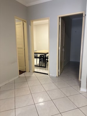 A hallway with tiled flooring leading to a dining area with a table and chairs.