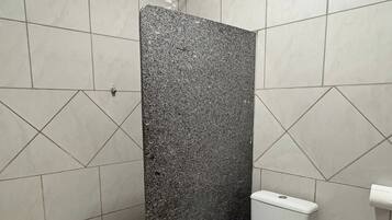 Ein Badezimmer mit Toilette, Dusche und einem schwarzen Mülleimer.