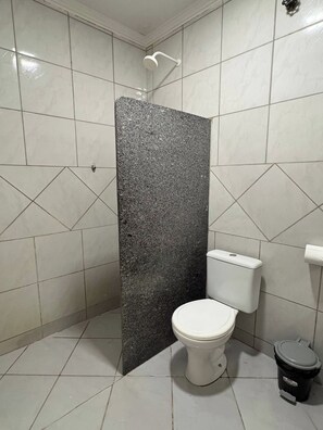 A bathroom with a white toilet, a shower, and a black trash bin. - Alameda House - 2 bedrooms and private garage (Mossoró)