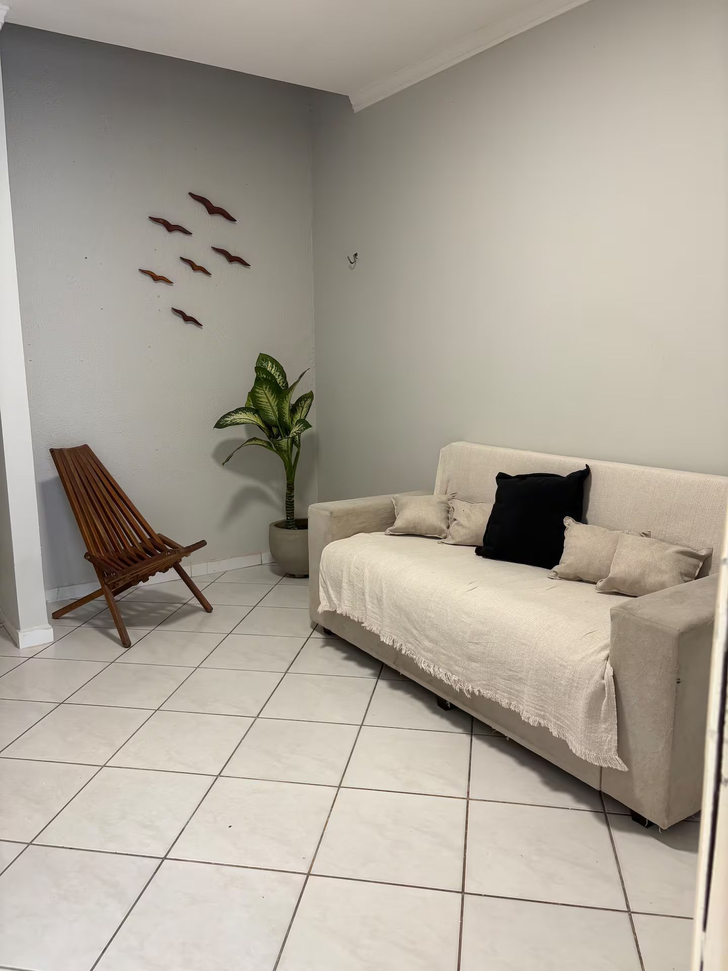 Sala de estar com sofá bege, cadeira de madeira, planta em vaso e obras de arte na parede.